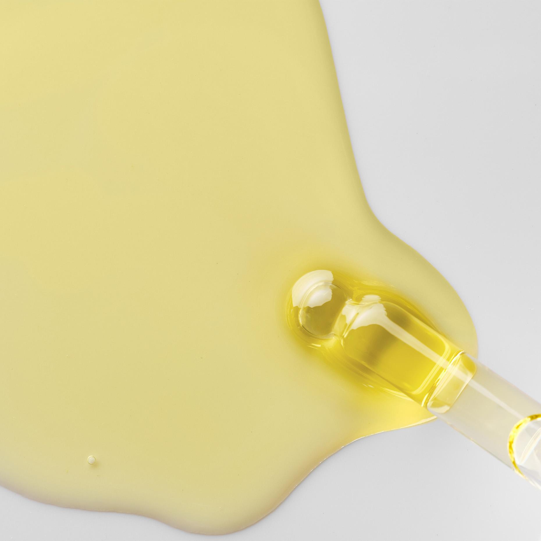 A dropper with yellow liquid spills onto a white surface